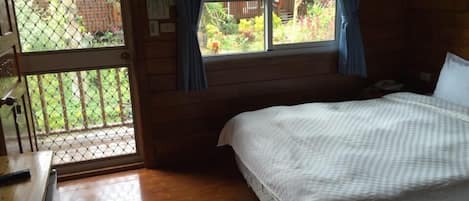 Una habitación de madera con una cama, un escritorio y una ventana que da a un jardín.