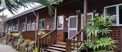 A wooden cabin with a porch, steps, and a small garden area with various plants.