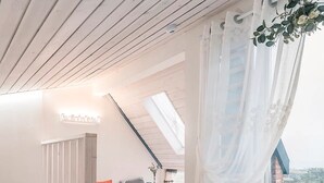 Quarto com teto inclinado, uma cama, escada e vista para o exterior.