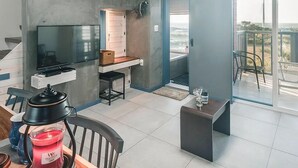 Uma cozinha moderna com televisão de tela plana, uma pequena área de jantar com mesa e cadeiras, e uma varanda com vista.