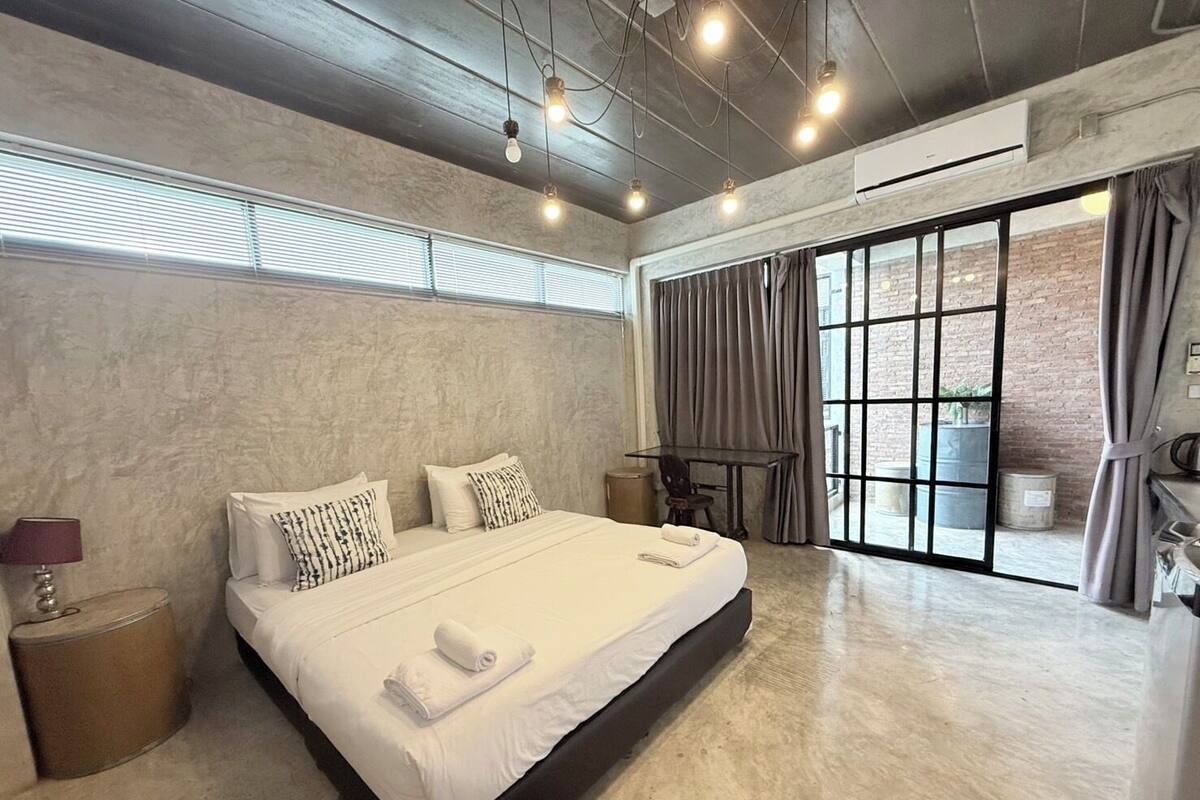 A modern hotel room with a large bed, a small table, and a view of the outdoors.