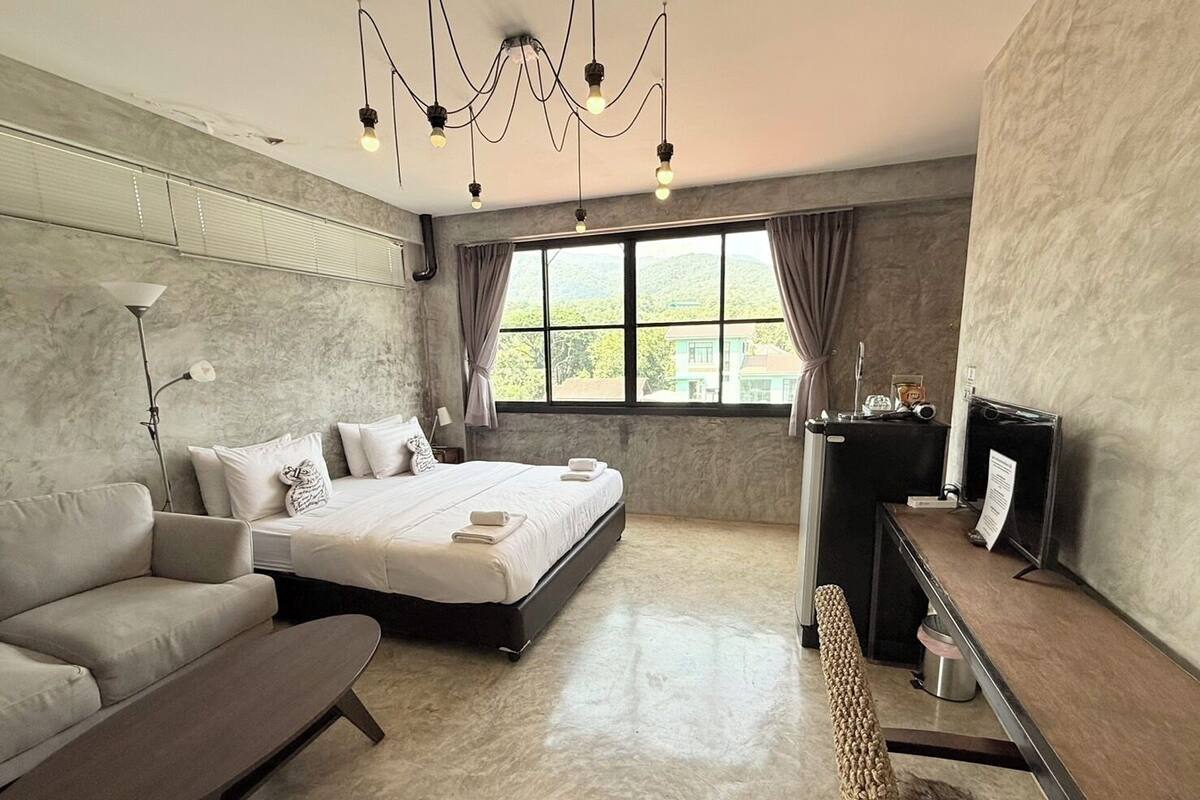 A modern hotel room with a bed, sofa, desk, and large window.