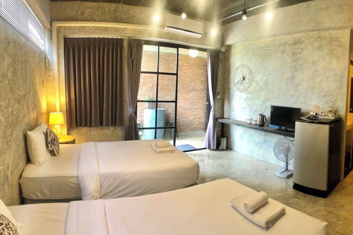 A hotel room with two beds, a desk, a TV, and a refrigerator.
