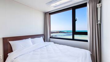A hotel room with a bed, a window with a view of the beach and ocean, and a ceiling light.