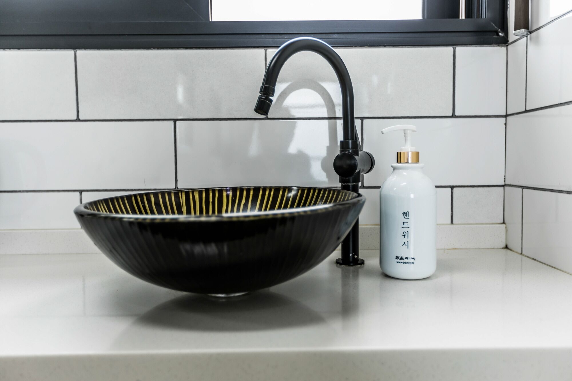 A black ceramic sink with a modern faucet and a white bottle of hand soap on a white countertop.