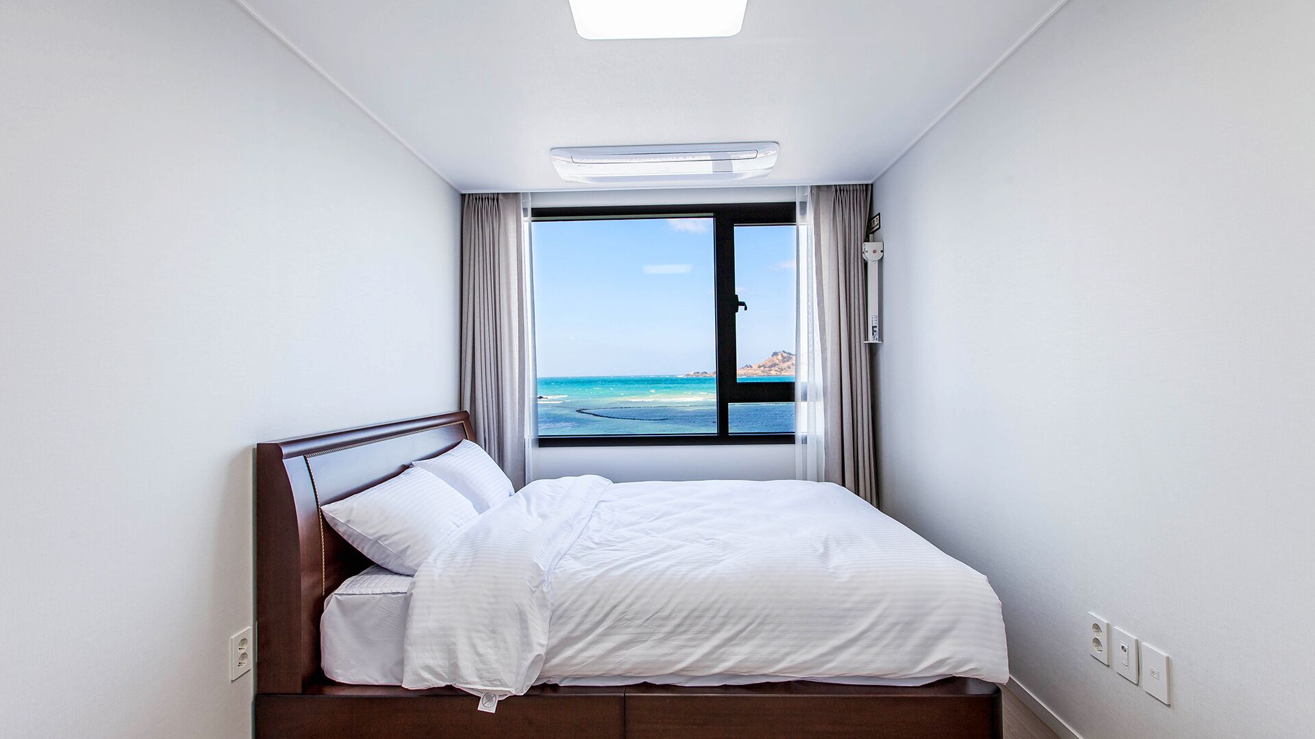 Ein Hotelzimmer mit Bett, Fenster mit Meerblick und Deckenleuchte.