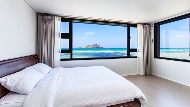 Un cuarto de hotel con una cama grande, vista a la playa y una montaña al fondo.