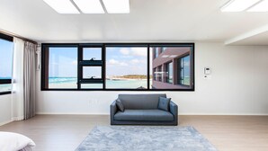 Una sala de estar moderna con un amplio ventanal que ofrece vista a la playa, un sofá gris y un tapete estampado.