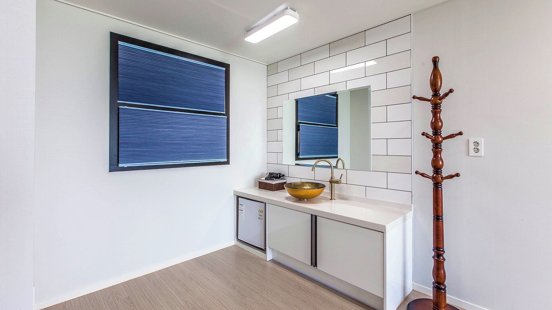 Un bagno moderno con un mobile lavabo bianco, un lavabo in ceramica dorato, uno specchio sopra il lavabo e un appendiabiti in legno.