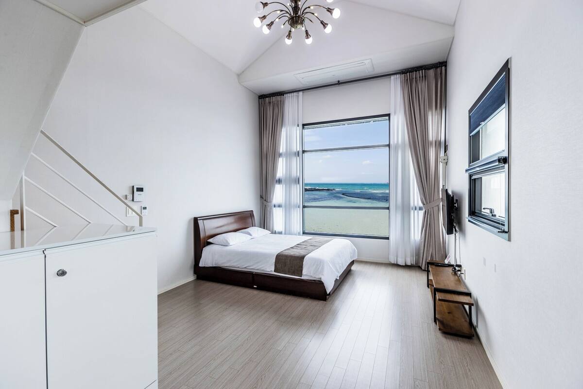 Ein modernes Schlafzimmer mit großem Fenster, einem Bett, einem Schreibtisch und einer Treppe.