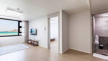 Een moderne hotelkamer met een groot raam met uitzicht op zee, een wandgemonteerde flatscreen-tv, een klein houten tafeltje en een aparte badkamer.
