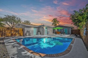 A backyard with a swimming pool, a house, and a wooden fence.