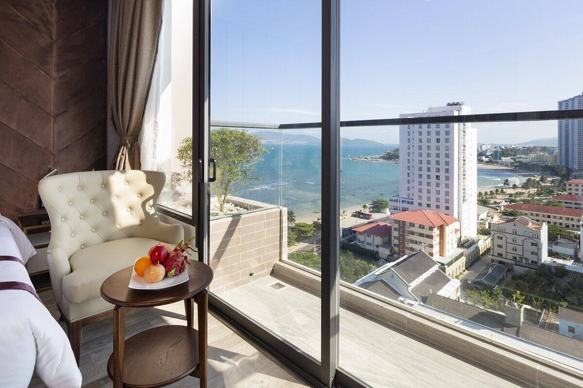 A hotel room with a large window overlooking a coastal cityscape.