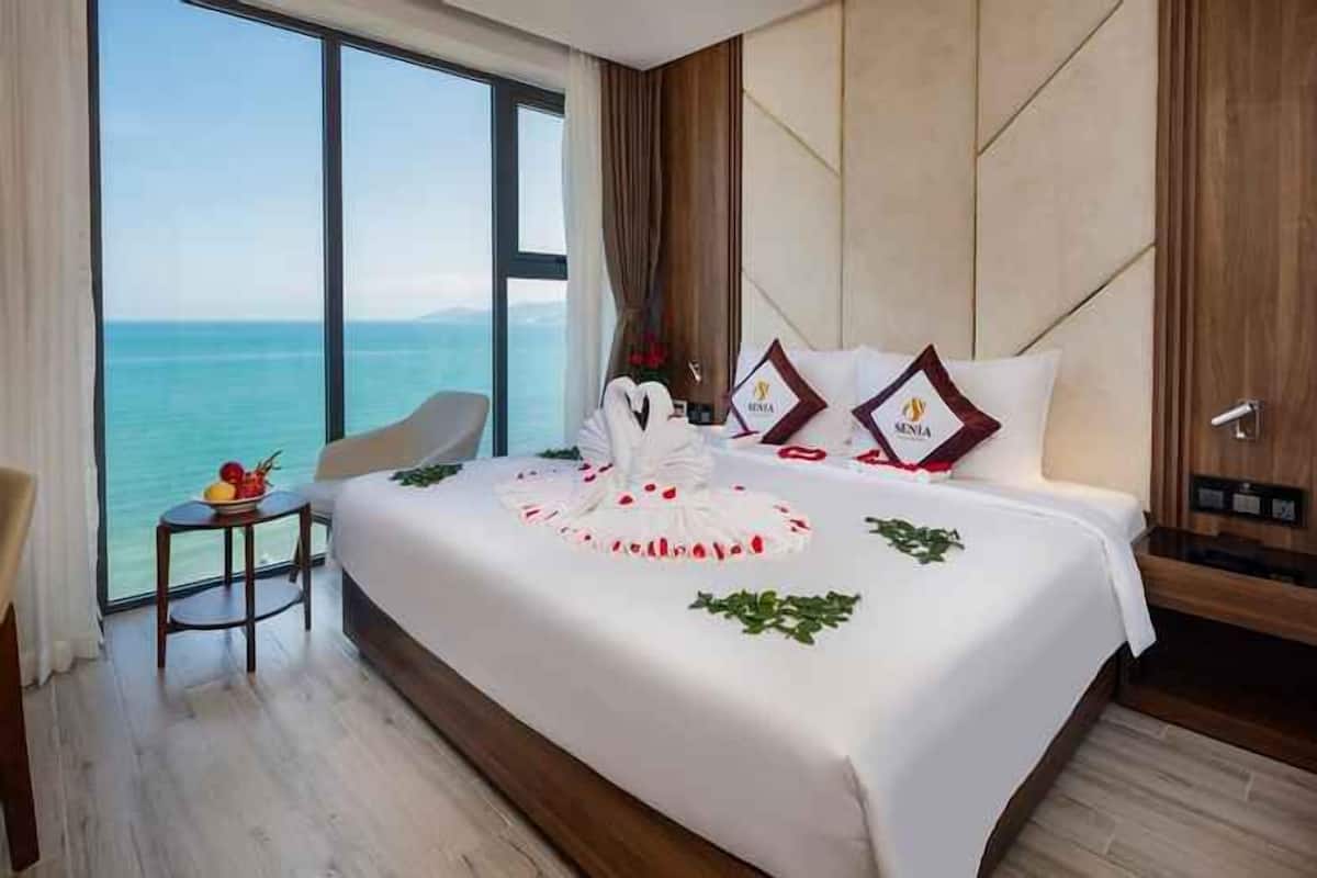 A hotel room with a large bed, a view of the sea, and a small table with fruit.