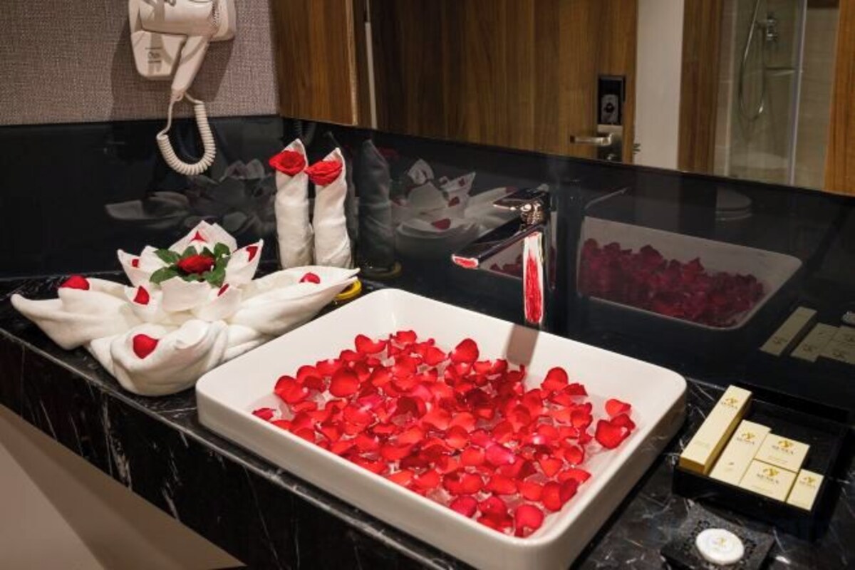 A bathroom with a black marble countertop, a white basin filled with red rose petals, and a white towel with a rose design.