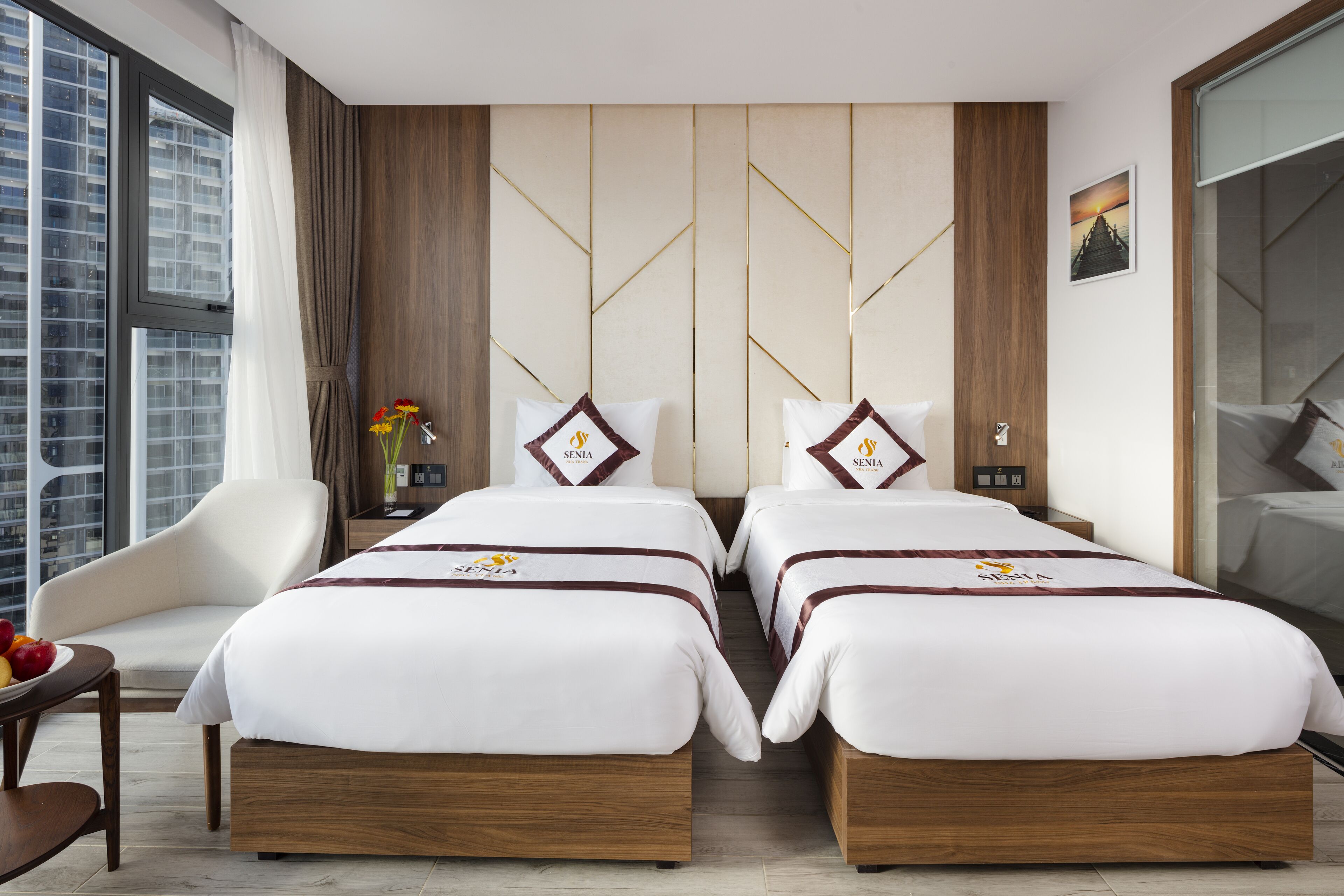 A hotel room with two beds, a sitting area, and a large window with a view of the city.