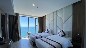 A hotel room with two beds, a desk, and a chair. The room has a large window with a view of the sea. - Senia Hotel (Bac Nha Trang)