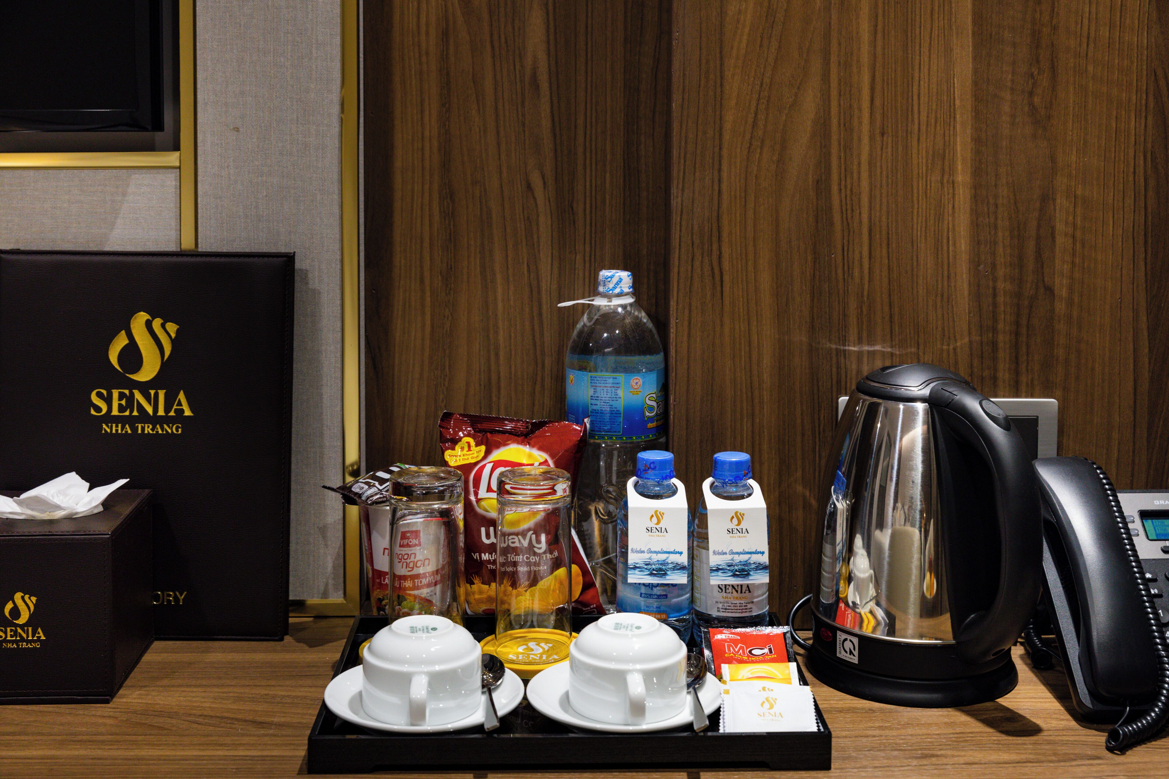 Disposição para o café da manhã em um quarto de hotel, incluindo cafeteira, chaleira e diversas bebidas.