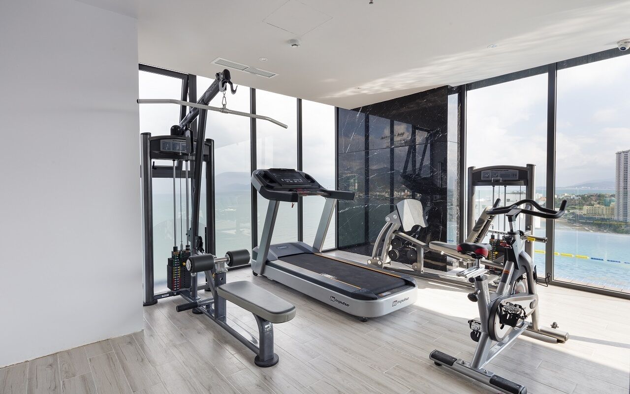 Et moderne fitnesscenter med løbebånd, crosstrainer og vægtmaskine, store vinduer med udsigt over byen.