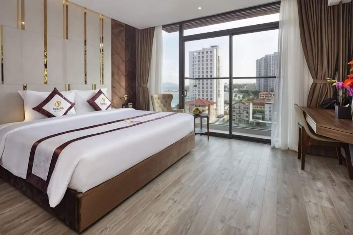 A hotel room with a large bed, a desk, and a view of the city.