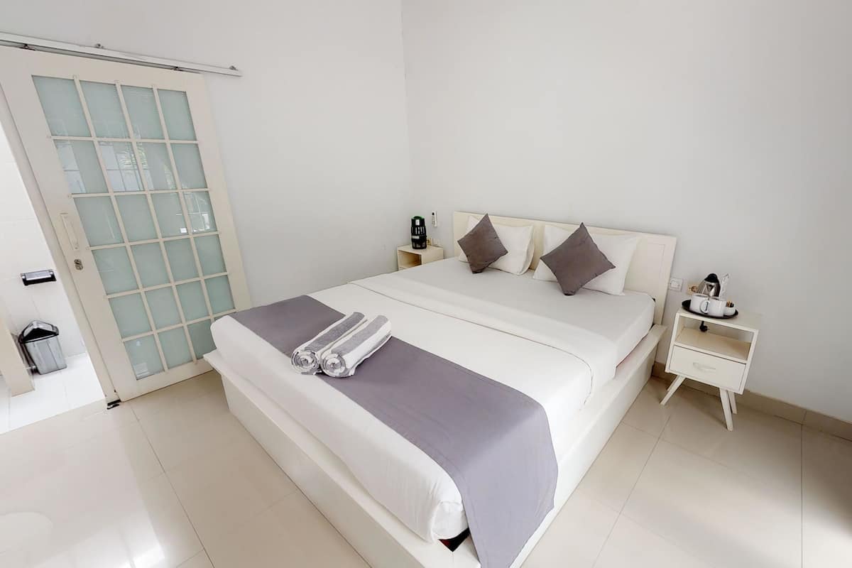 Ein Hotelzimmer mit einem Bett, einem Nachttisch, einem kleinen Tisch, einem Mülleimer und einer Schiebetür mit satinierten Glasscheiben.