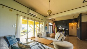 A living room with a sofa, armchair, coffee table, and a bookshelf. - Panorama (Yomitan)