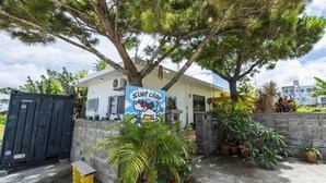 A house with a 'Surf Camp' sign, surrounded by potted plants and a concrete wall. - Panorama (Yomitan)