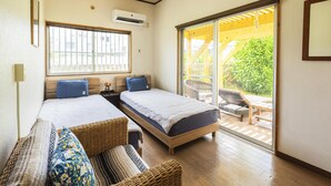 A bedroom with two beds, a large window, and a sliding glass door leading to an outdoor area with a wooden deck and chairs. - Panorama (Yomitan)