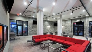 Un espace de détente moderne avec un canapé d’angle rouge, des tables et des chaises, de grandes fenêtres et un mur en pierre.