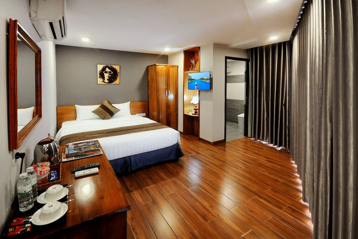 Une chambre d’hôtel avec un lit, un plancher en bois, une télévision, un bureau avec une lampe et un miroir.