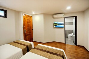 A hotel room with two beds, a wooden door, a TV on the wall, and an air conditioning unit.