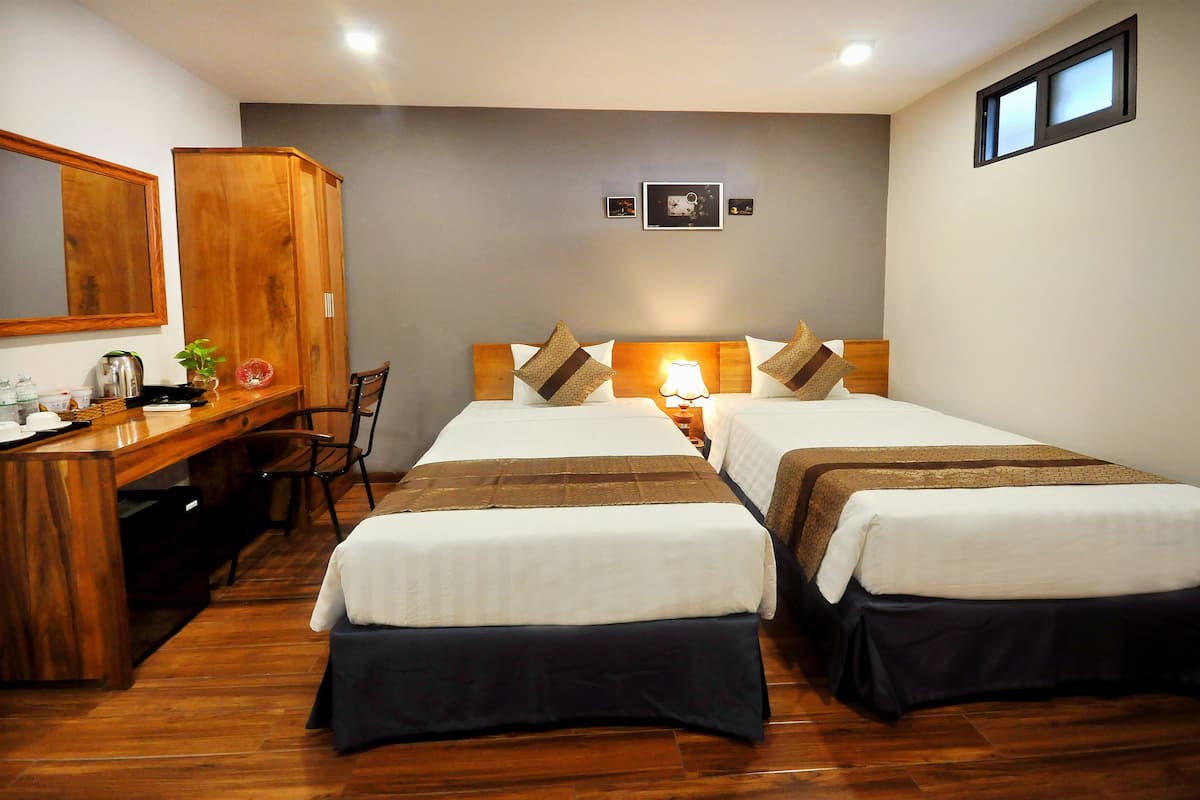 Une chambre d’hôtel avec deux lits, un bureau en bois, une chaise et un miroir.