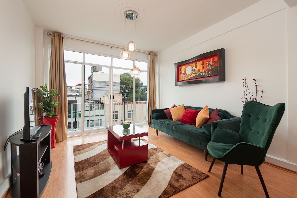 A modern living room with a sofa, a coffee table, a TV stand, and a large window with curtains.