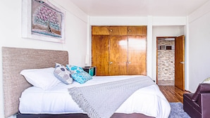 A bedroom with a bed, a wooden wardrobe, a glass table, and a painting on the wall. - Roma Sur Balcony Apartments - Family Friendly (Mexico City)