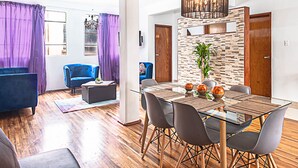 A modern living room with a glass dining table, blue sofas, and a chandelier. - Roma Sur Balcony Apartments - Family Friendly (Mexico City)