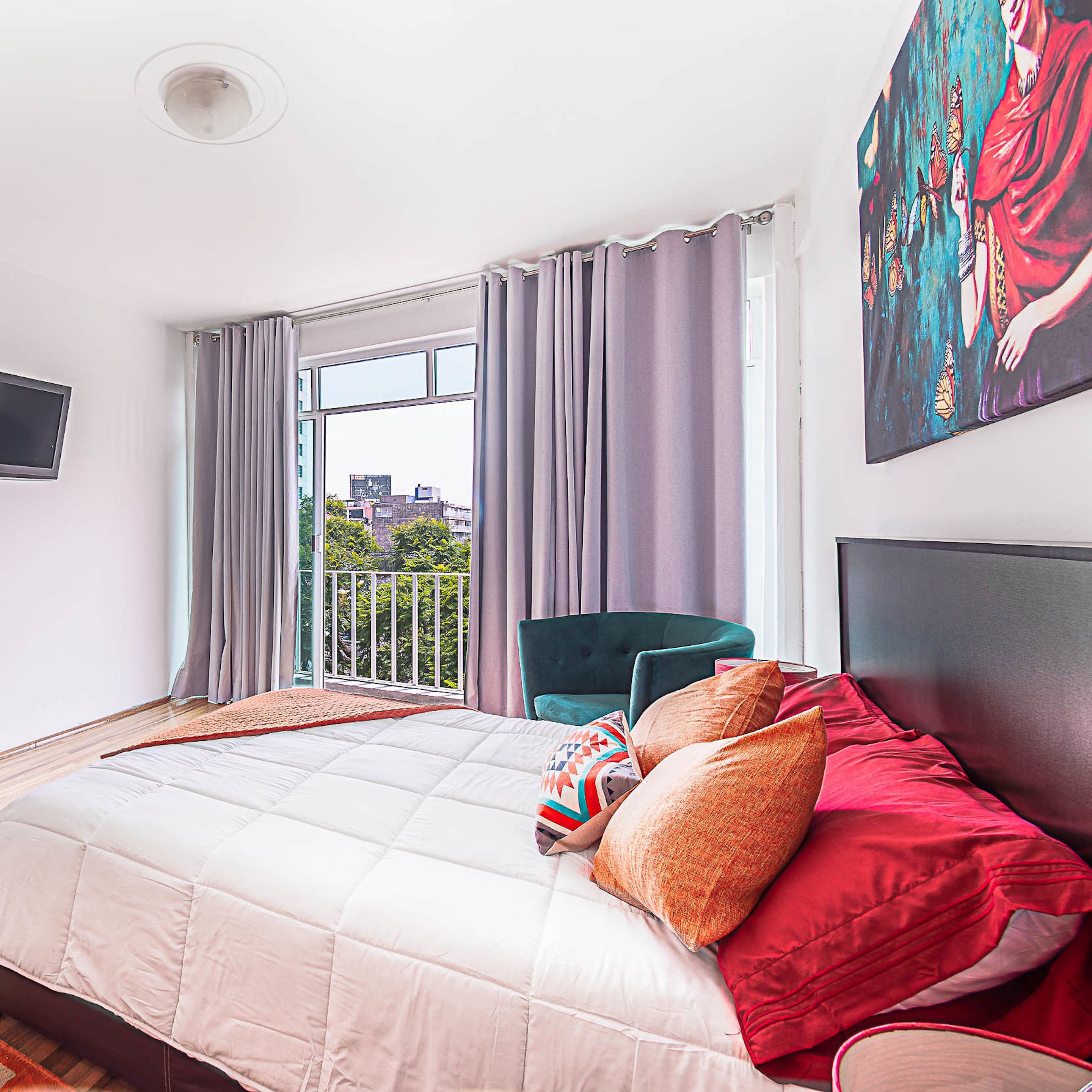A bedroom with a large bed, a chair, a painting, and a window with curtains.