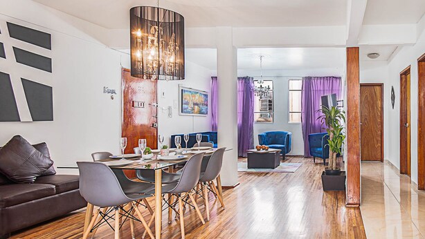 A modern living room with a dining area, wooden flooring, and contemporary furniture. - Roma Sur Balcony Apartments - Family Friendly (Mexico City)