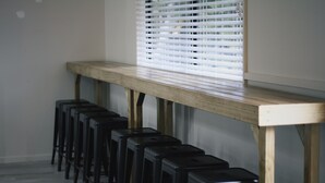 A row of black bar stools aligned against a wooden bench and a window with blinds.
