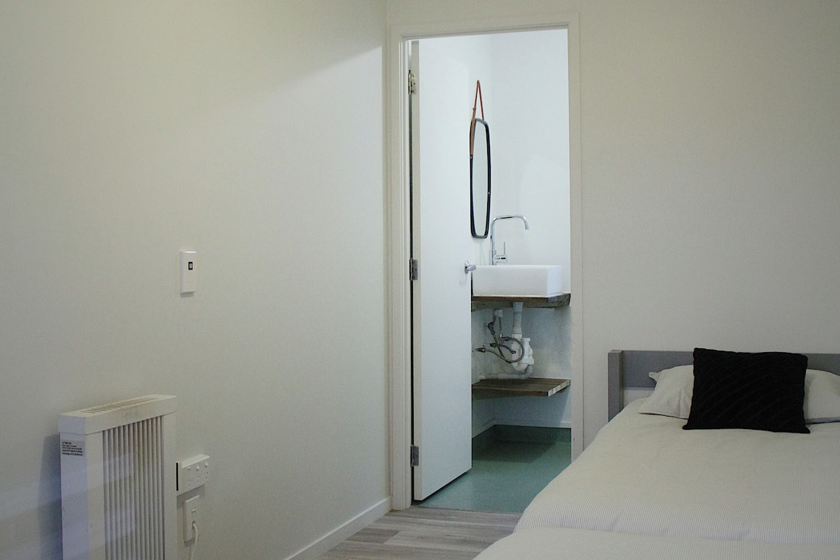 A bedroom with a bed, a radiator, a door leading to a bathroom, and a ceiling light.