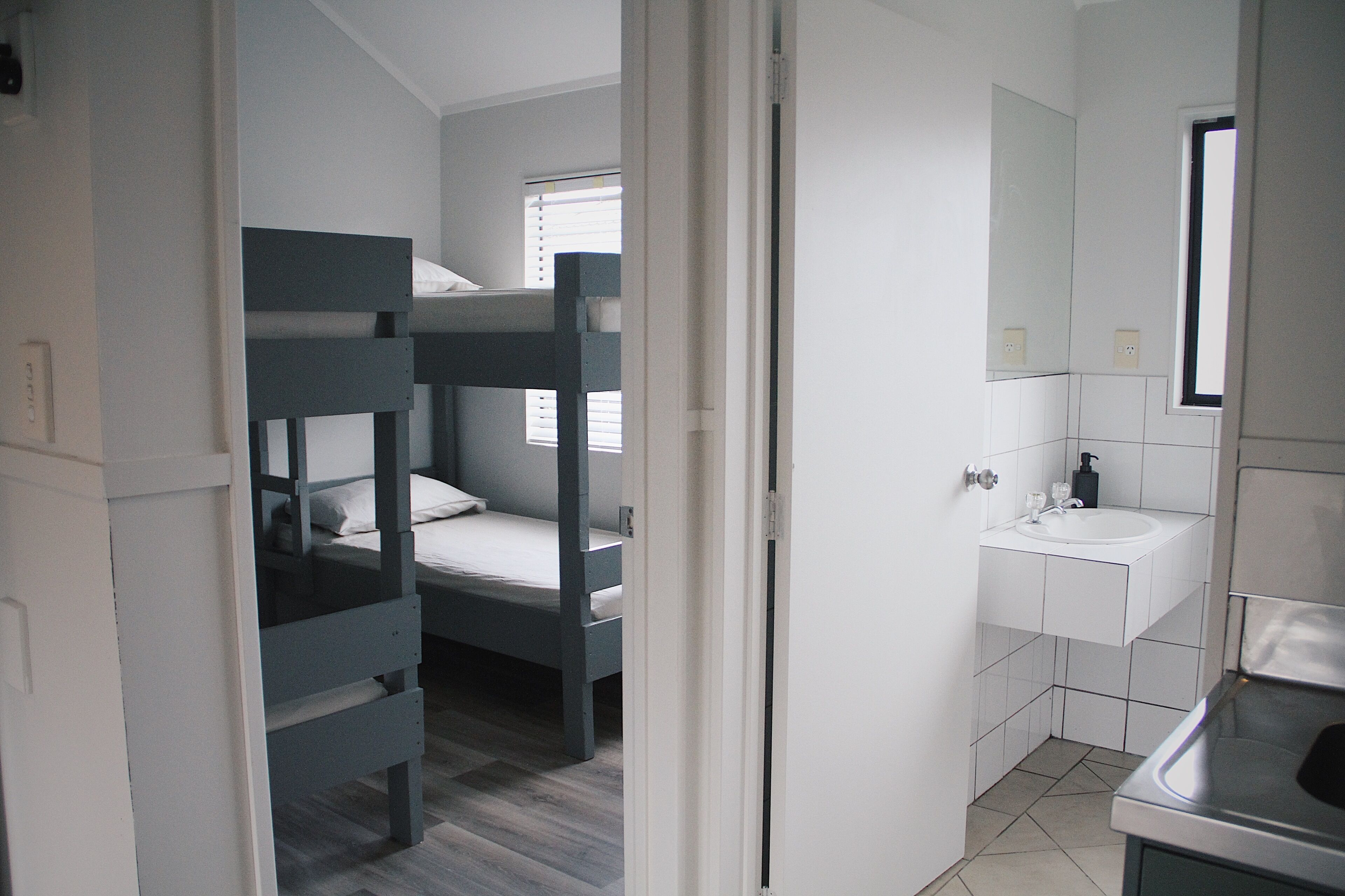 Una habitación con literas, baño con lavabo y espejo, y ventana con persianas.