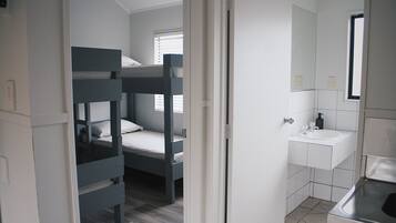 Una habitación con literas, baño con lavabo y espejo, y ventana con persianas.