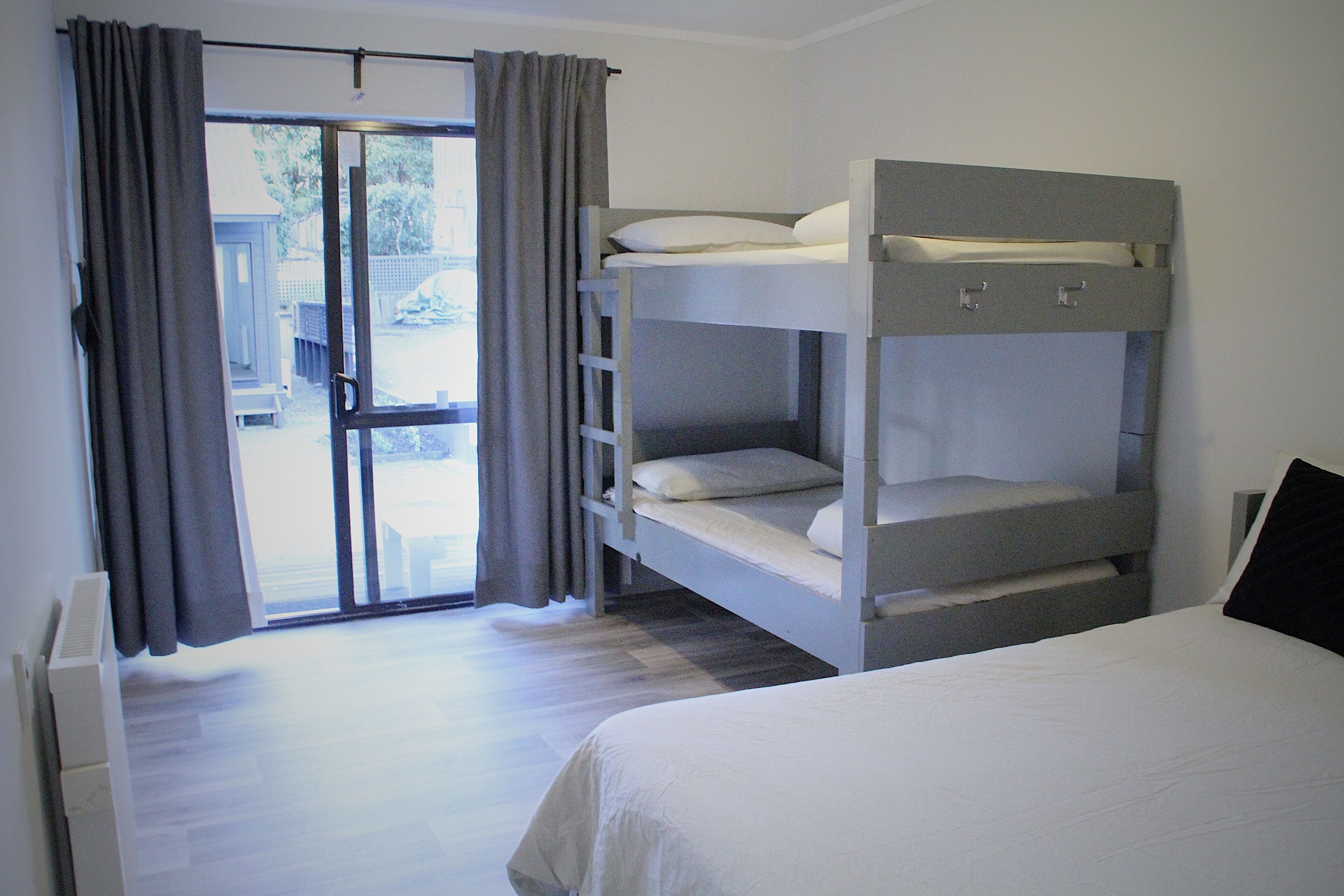 A room with a bunk bed, a single bed, and a sliding glass door leading to an outdoor area.
