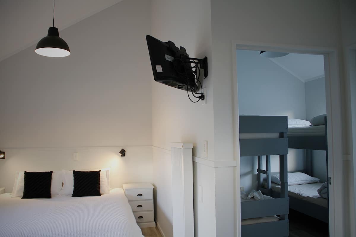 A bedroom with a single bed, a bedside table, a lamp, and a TV mounted on the wall.