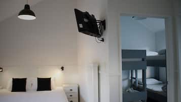 A bedroom with a single bed, a bedside table, a lamp, and a TV mounted on the wall.