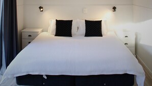 A modern bedroom with a large bed, bedside tables, a hanging light fixture, and a window with curtains.
