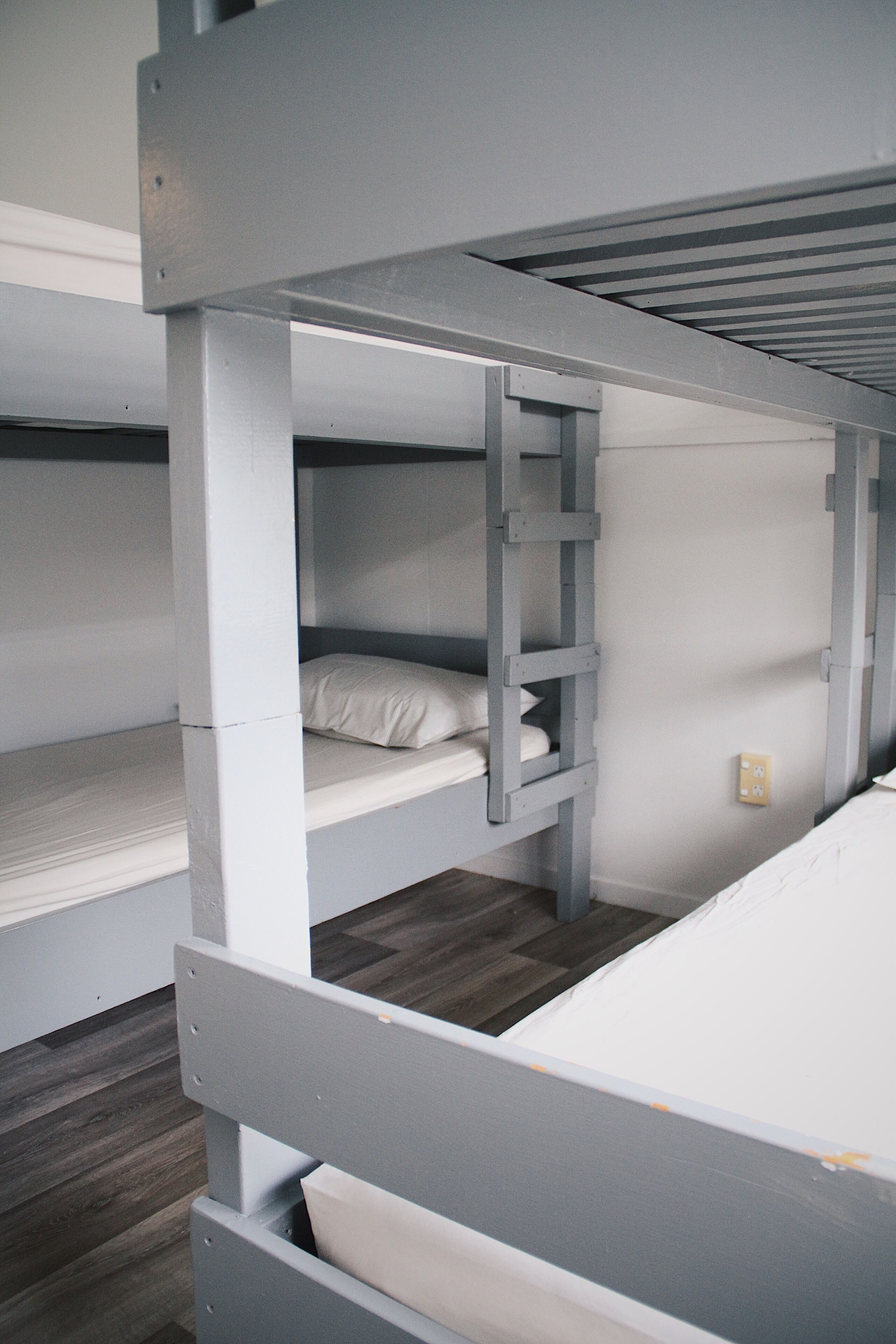 A bunk bed with a ladder, a white mattress, and a wooden floor.