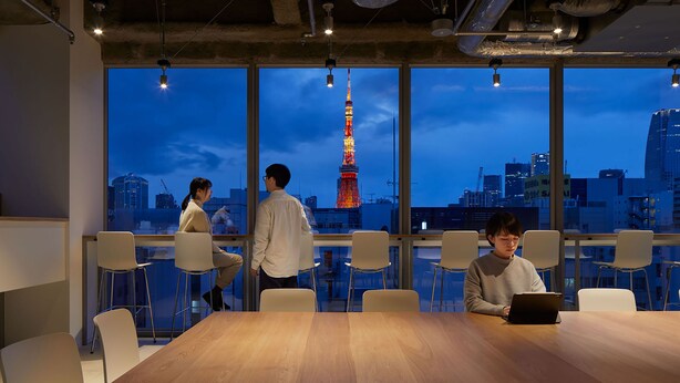 A conference room with a large table and chairs, large windows with a cityscape view including a tower, and visible ceiling pipes. - 9h nine hours Hamamatsucho (Tokyo)
