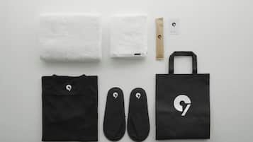 Una bolsa de tela negra, un par de zapatillas negras, una camiseta negra, dos toallas blancas, una bolsa de papel marrón y una tarjeta con un logotipo.
