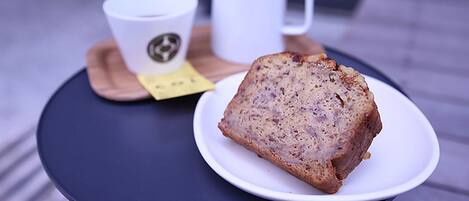 A slice of bread on a white plate on a round table, a white mug, and a coaster with a logo.