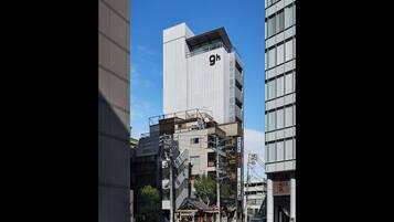 A modern urban street with tall buildings, a traditional wooden structure, and pedestrians.